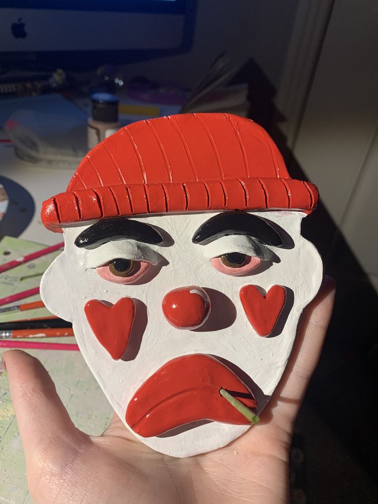 a person holding up a mask that looks like a clown's face with hearts on it