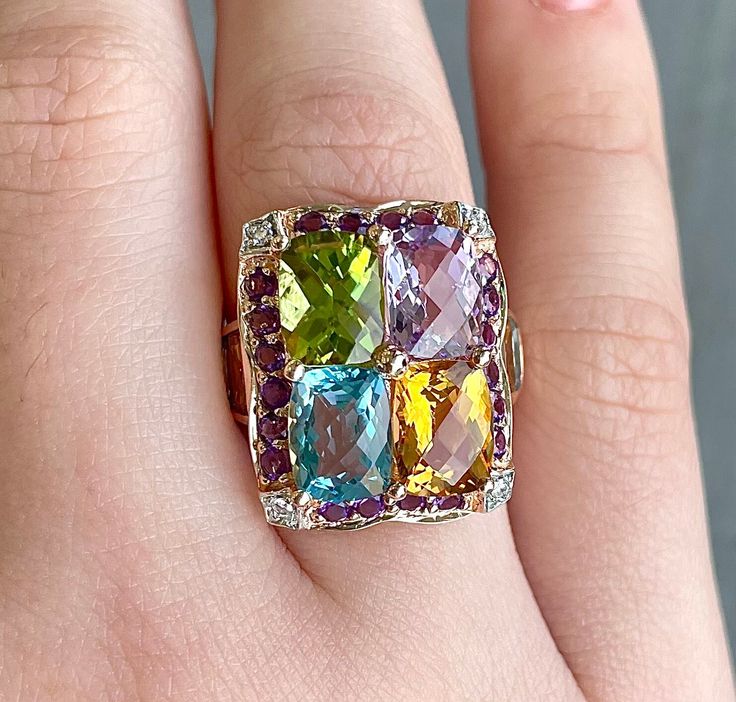 A multicolored gemstone ring, that is VERY. HEAVY on the gemstones, 14k Rose Gold, currently a size 5 1/4. The Gemstones are Blue Topaz, Citrine, Peridot, and Amethyst. There are 2 more citrine, and 2 blue topaz on the sides of the band. There is a darker purple amethyst halo around the large stones with 4 small diamond accents in the corners with white gold prongs on the small diamonds. 1x 6.0x7.5mm cushion cut light amethyst 1x 6.0x7.5mm cushion cut citrine 1x 6.0x7.5mm cushion cut blue topaz 1x 6.0x7.5mm cushion cut peridot 2x 5.0x2.9mm tapered rectangle citrine 2x 4.2x2.4mm tapered rectangle blue topaz 4x 1.2mm round diamonds 20x 1.6 round dark amethyst Luxury Multicolor Multi-stone Gemstones, Luxury Multicolor 14k Gold Gemstones, Multicolor Diamond Gemstones With Accents, Luxury Multicolor Gemstones With Accents, Fine Jewelry Multicolor Oval Gemstones, Oval Multicolor Diamond Gemstones, Luxury Multicolor Gemstones, Formal Multicolor Fine Jewelry Gemstones, Luxury Multicolor Rings With Gemstone Accents