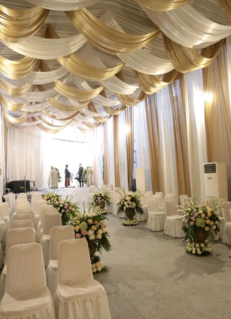 a banquet hall decorated with white and gold draping, flowers and chairs for an event