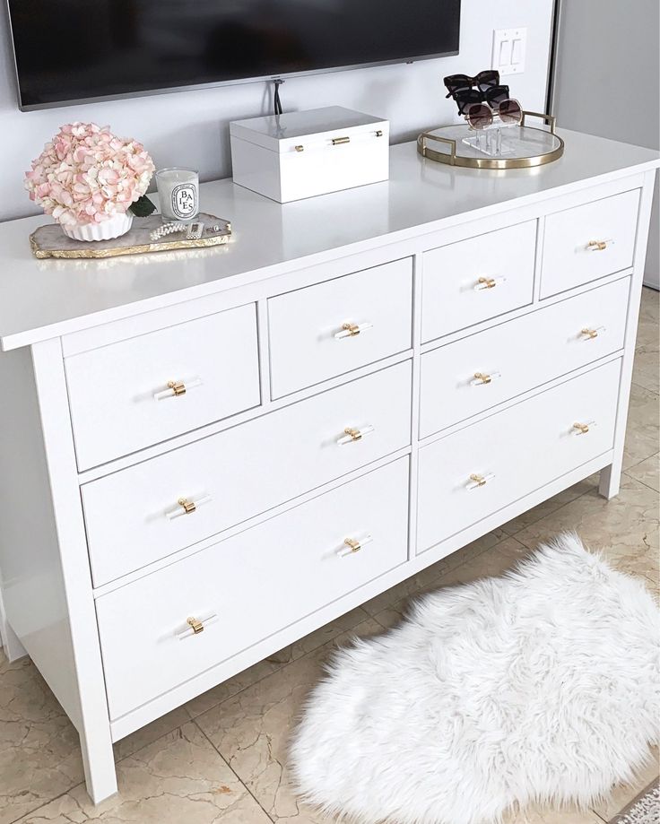 a white dresser with a large flat screen tv mounted above it and a rug on the floor