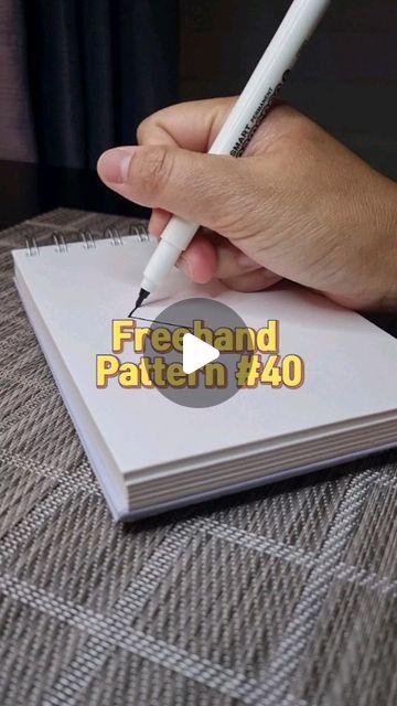 a person holding a pen and writing on top of a white book with the words freehand pattern & 40