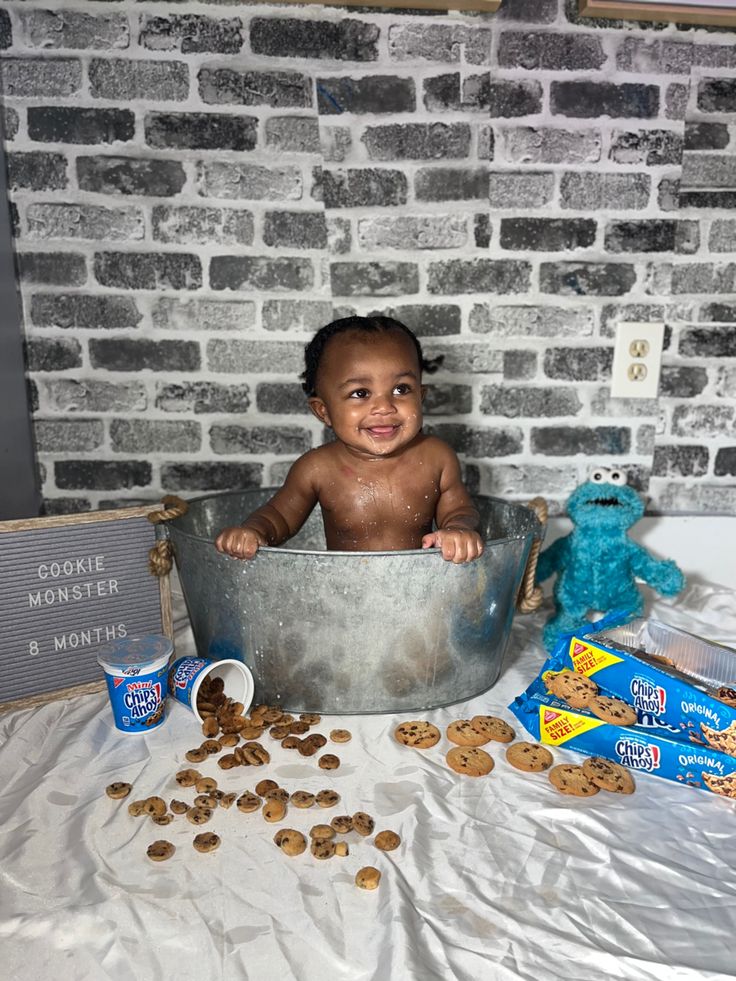 a baby sitting in a metal tub surrounded by cookies and other items on a table