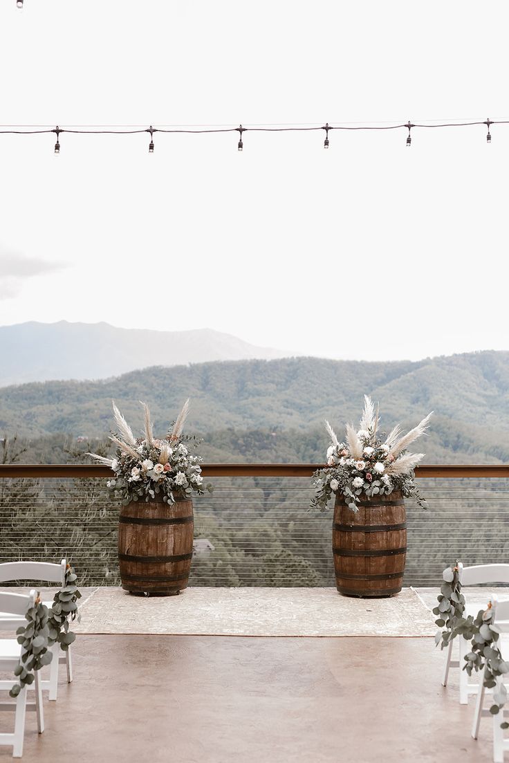 an outdoor ceremony setup with chairs and flowers in wooden barrels on top of a mountain