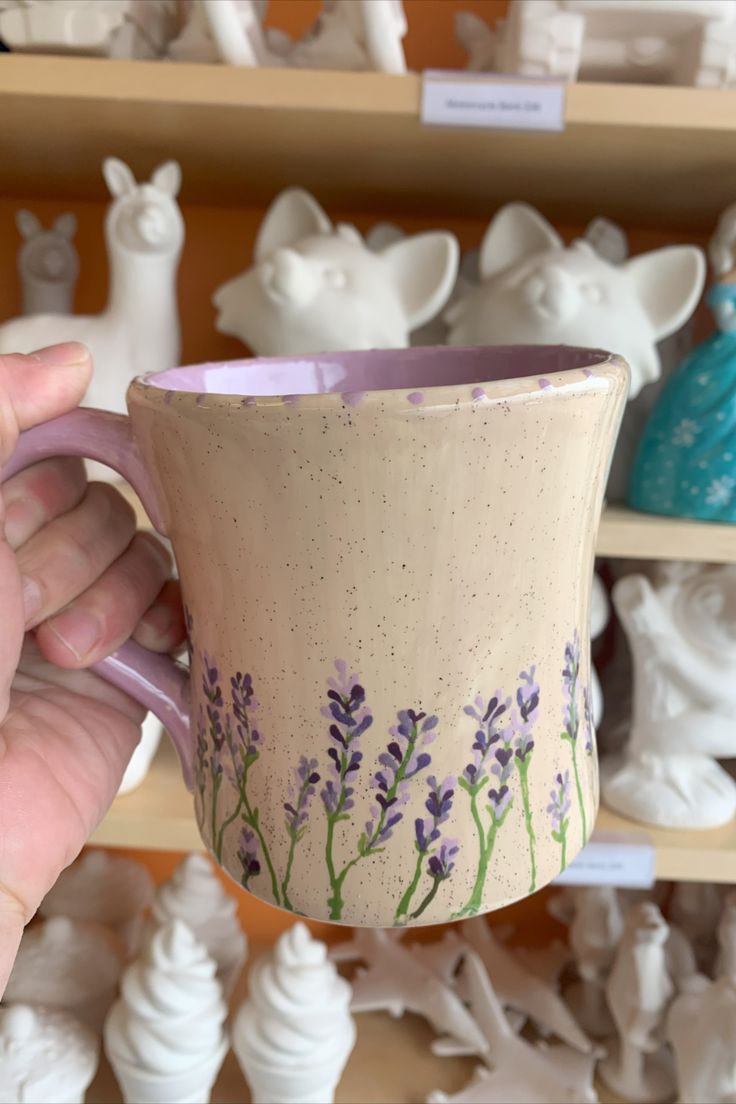 a hand holding a coffee cup with lavender flowers painted on the outside and inside it