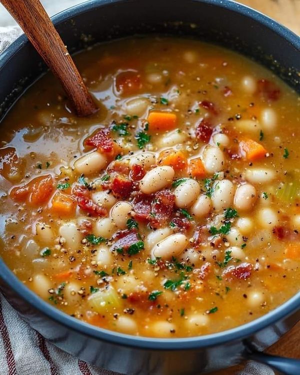 a bowl of soup with beans, bacon and parsley in it on a wooden table