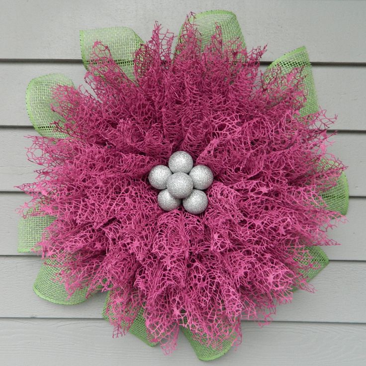 a pink and green wreath with three balls on it's center piece, hanging from the side of a house