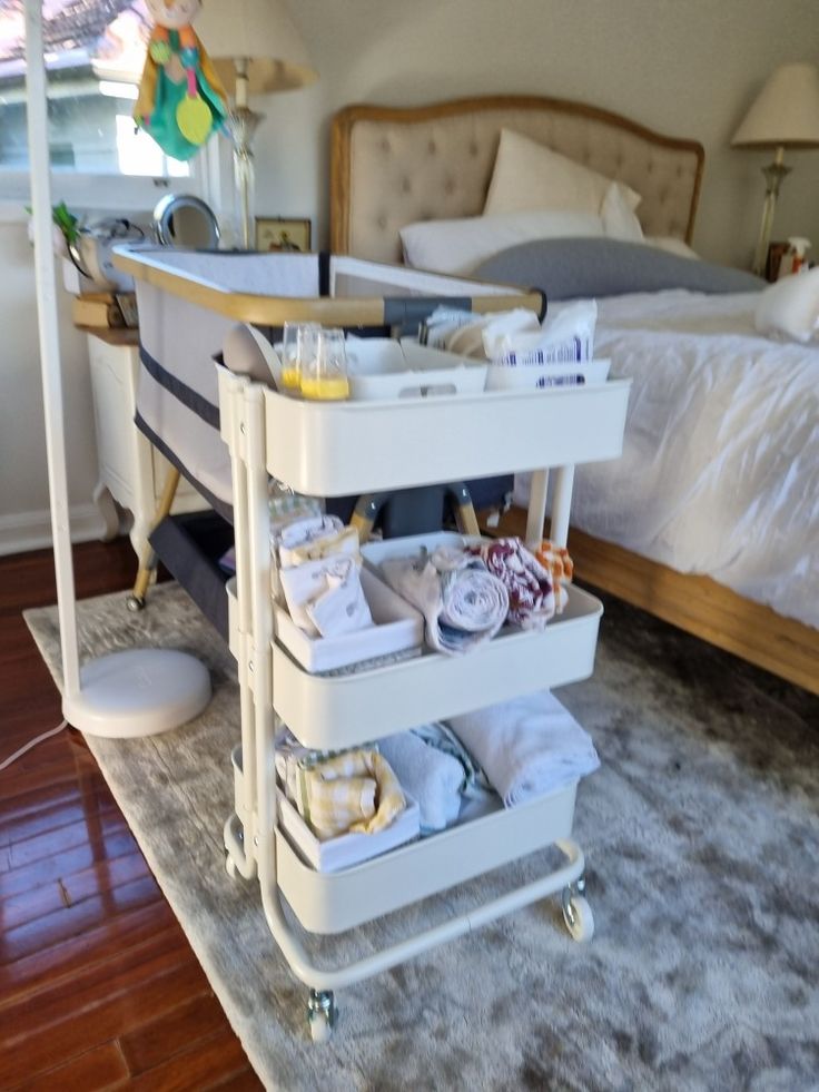 a bed room with a neatly made bed and a rolling cart on the floor next to it