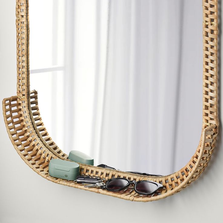 a wicker mirror with sunglasses and other items in front of it on a white wall