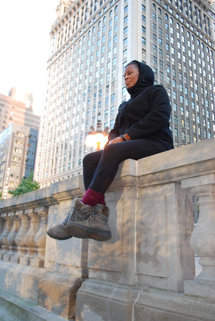 a woman sitting on top of a stone wall next to a tall building in the city