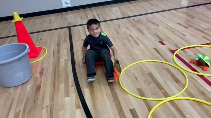 a young boy sitting on top of a wooden floor next to a bucket and hoop