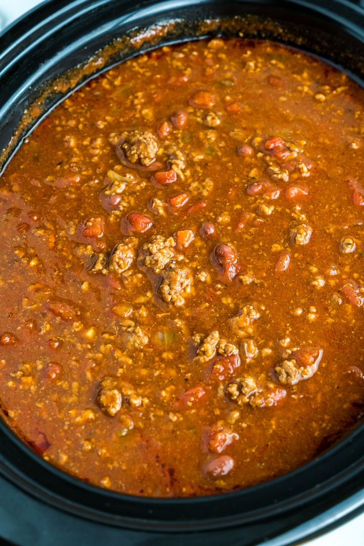 a slow cooker filled with chili and meatballs on top of a white table