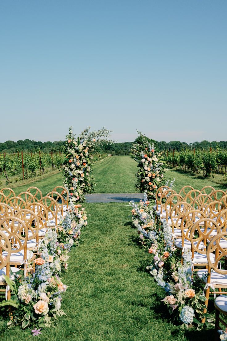 an outdoor ceremony set up with chairs and flowers on the aisle, surrounded by greenery