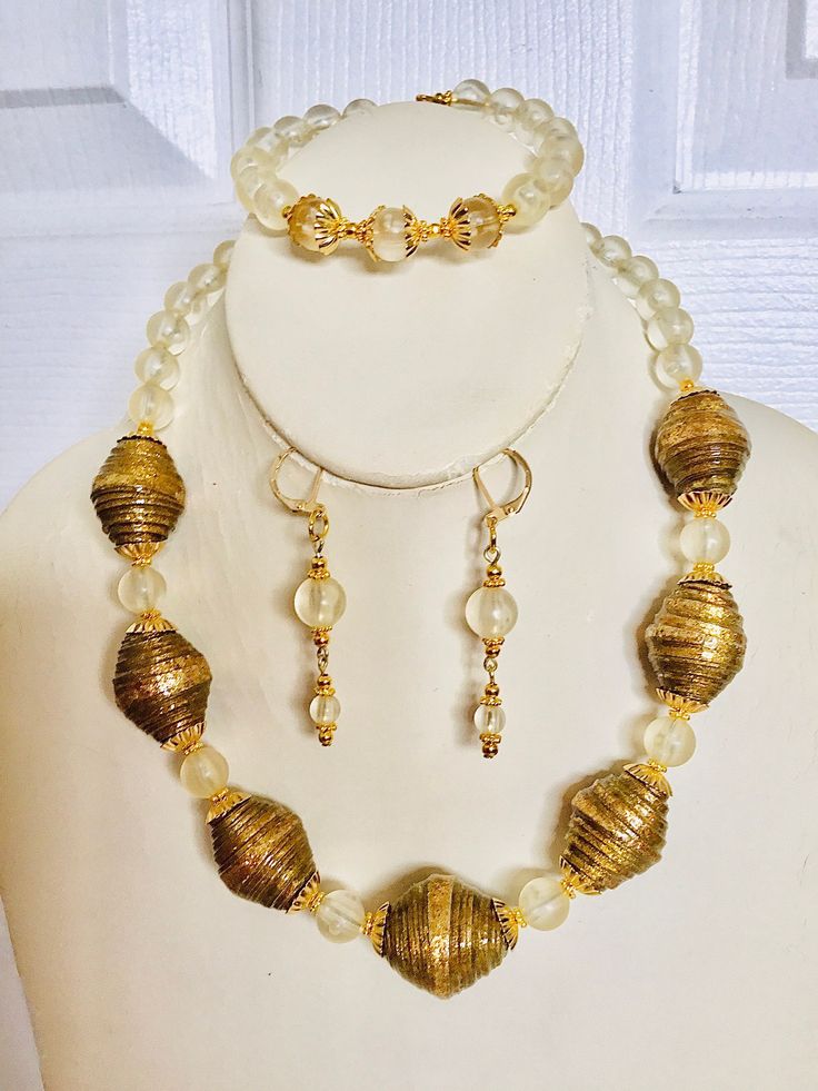 "Oval-shaped chunky gold paper beads, light gold frosted rounded acrylic beads, gold-tone bead caps, and tiny flat flower spacer beads are strung together with beading wire to create this lovely set. Avoid contact with water. Necklace 18\" long Bracelet cuff Earrings 2\" long" Adjustable Gold Necklace With Large Beads, Gold Metal Beads With Large Beads, Large Gold Beads For Costume Jewelry, Adjustable Gold Beaded Necklaces With Large Beads, Vintage Gold Beads For Festive Occasions, Adjustable Gold Beaded Necklace With Large Beads, Gold Necklaces With Polished Metal Beads, Festive Vintage Gold Beads, Gold Metal Beads Necklace For Jewelry Making