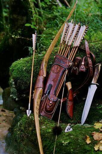 a bow and arrow laying on the ground next to some mossy rocks with water in the background