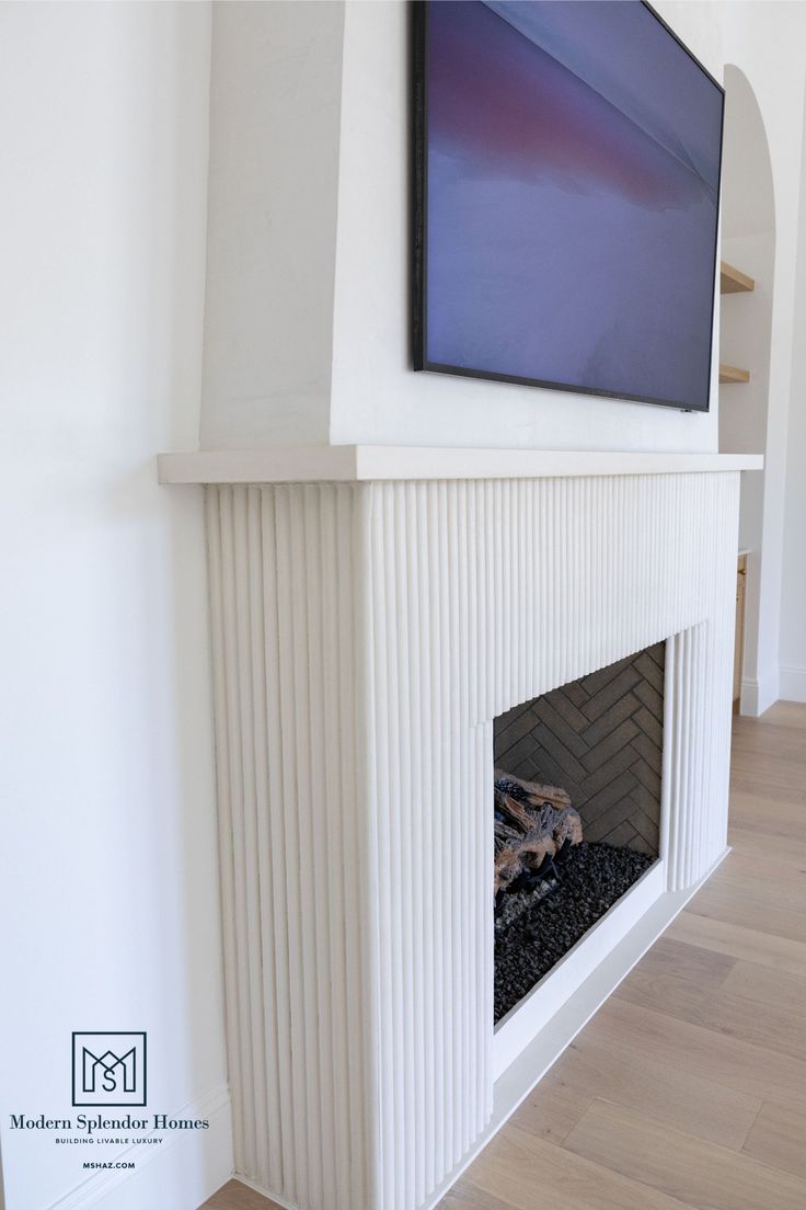 a flat screen tv mounted on the wall above a fireplace in a room with hardwood floors