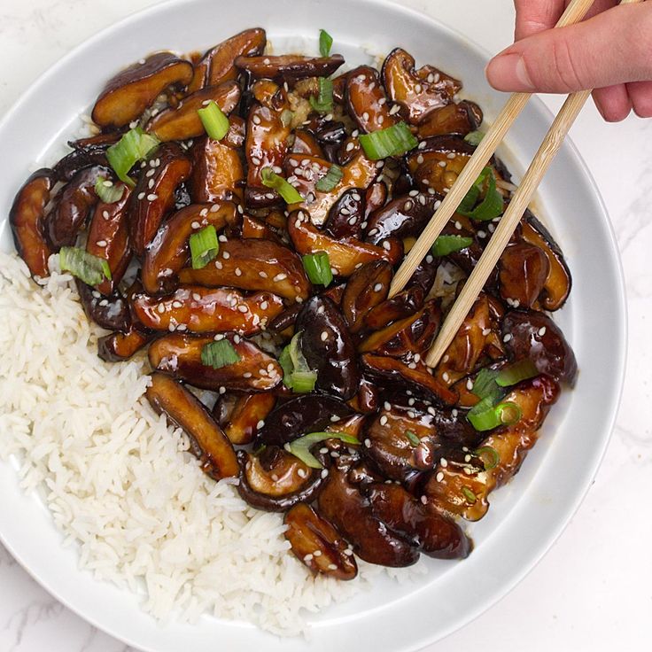 someone is holding chopsticks over a plate of rice with mushrooms and green onions