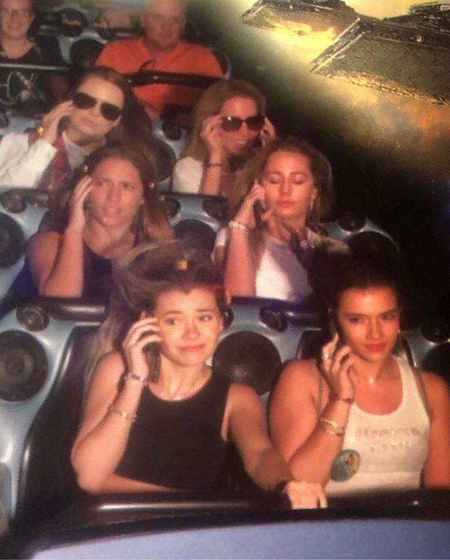 several people sitting in a roller coaster talking on their cell phones