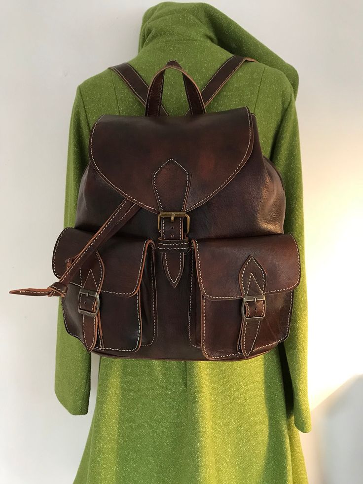 "Handmade brown leather rucksack. Unisex  Simple but yet stylish leather rucksack made of vegetable tanned sheep skin . Perfect for traveling or to take to school or work . Medium size rucksack   Front pockets Back zip pocket  Inside zip pocket  Inside lining  Top handle  Real buckle for opening  Adjustable shoulder strap Dimensions: W: 11\" H : 13\" D : 6\" Please kindly note! Natural variation in leather is not considered damages but it is part of natural beauty and character of the leather. W Brown Leather Backpack For Travel, Brown Leather Travel Backpack, Adventure Leather Satchel Backpack With Leather Backing, Leather Satchel Backpack For Adventure, Vintage Leather Backpack For School With Leather Lining, Adventure Leather Satchel Backpack, Classic Leather Adventure Backpack, Brown Soft Leather Satchel Backpack, Brown Soft Leather Backpack