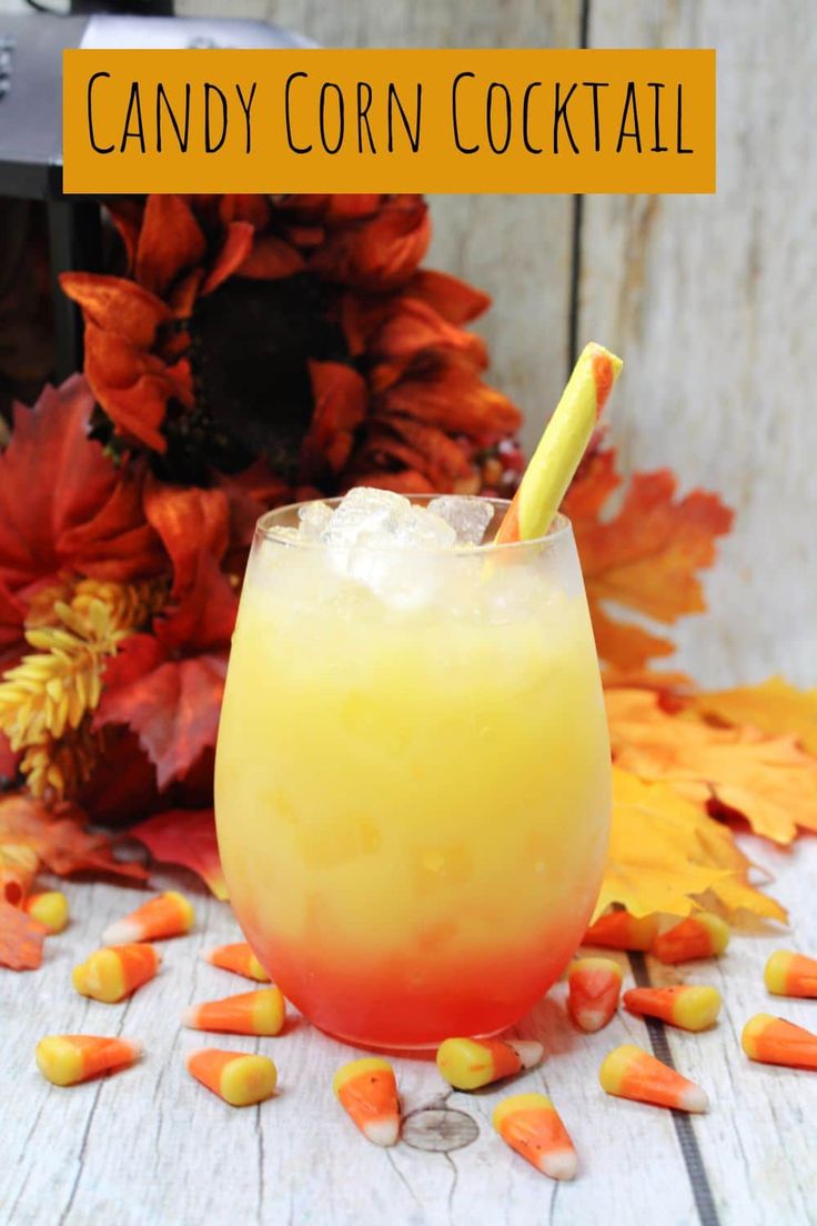 a glass filled with candy corn cocktail on top of a wooden table next to fall leaves