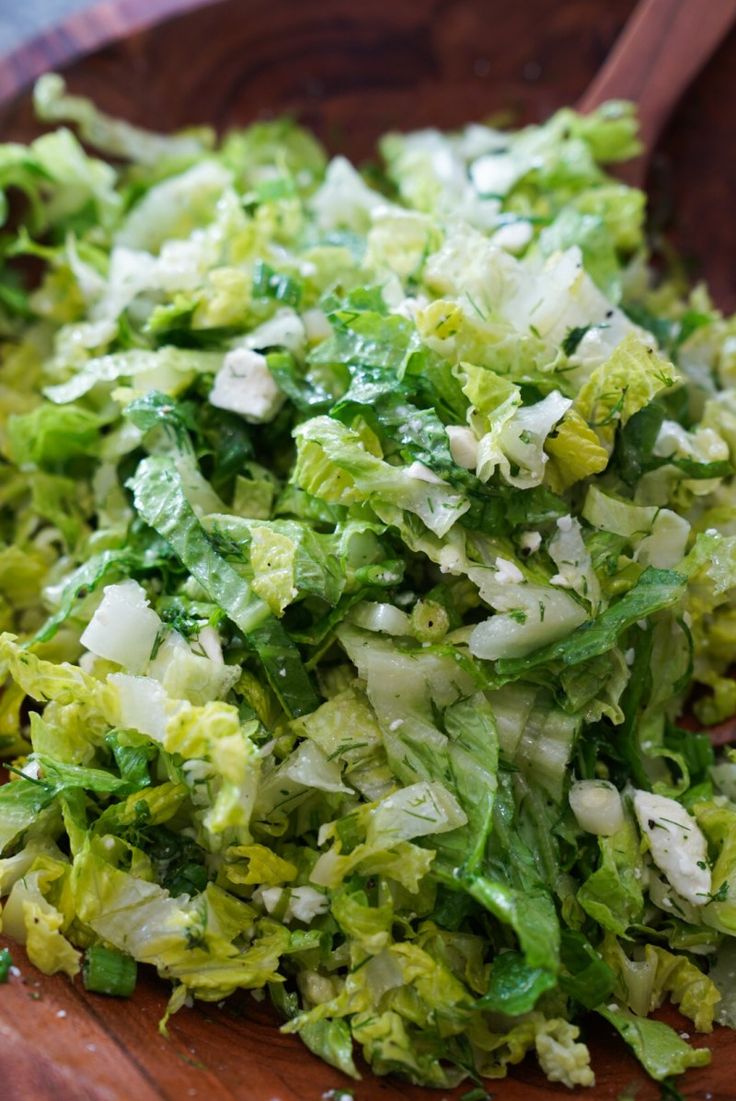 a wooden bowl filled with lettuce on top of a table next to a spoon