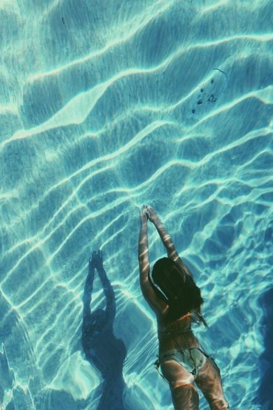 a woman swimming in a pool with her shadow on the water's surface,