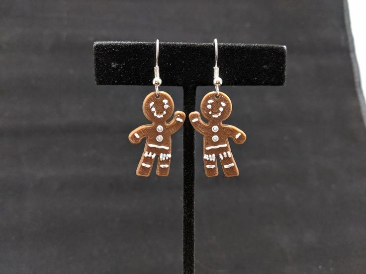 two gingerbread men earrings are on a black display stand and one is wearing a gold plated earring