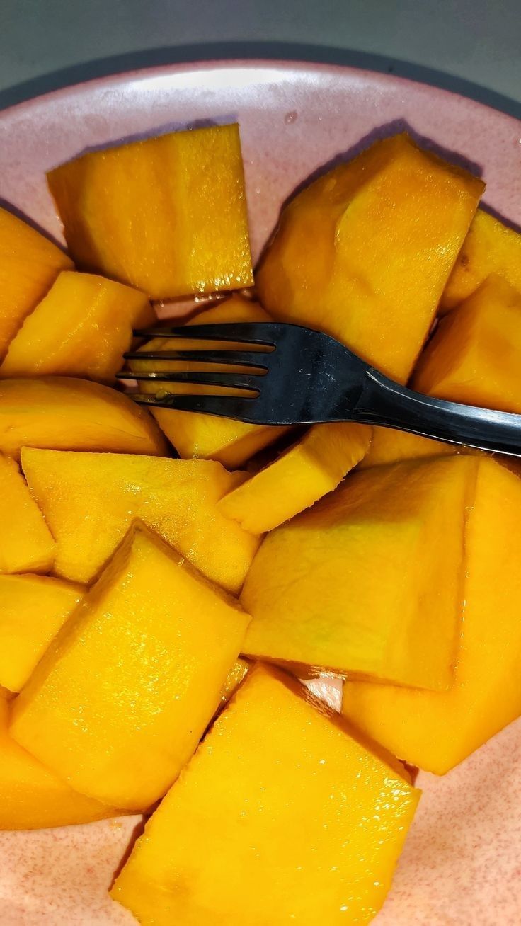 a fork is stuck into some cut up mangoes on a pink and white plate