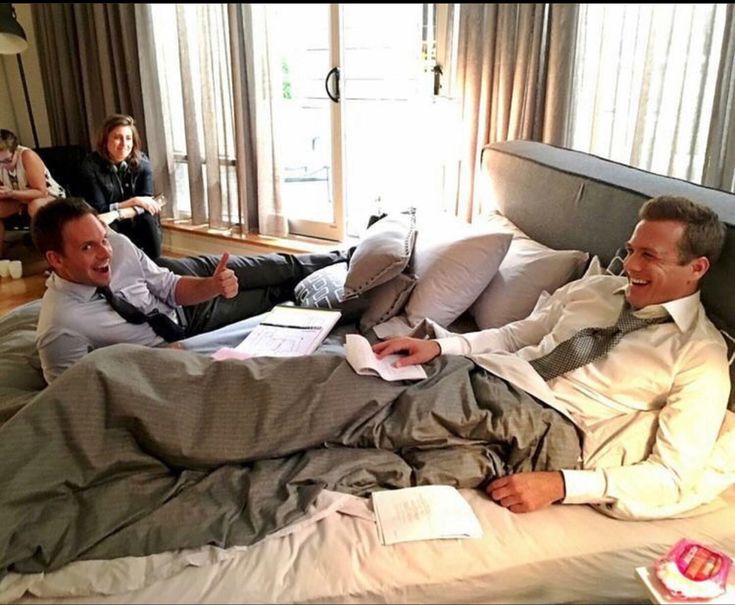 two men in suits are laying on a bed and one man is pointing at something