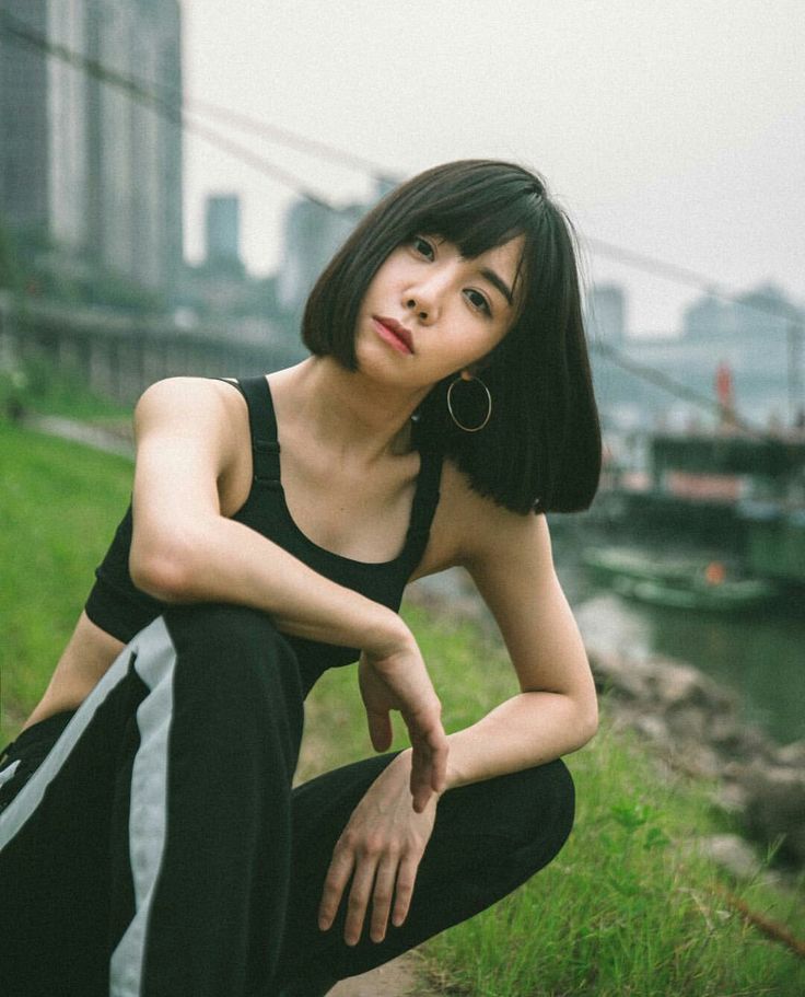 a woman sitting on the ground in front of a body of water with buildings in the background