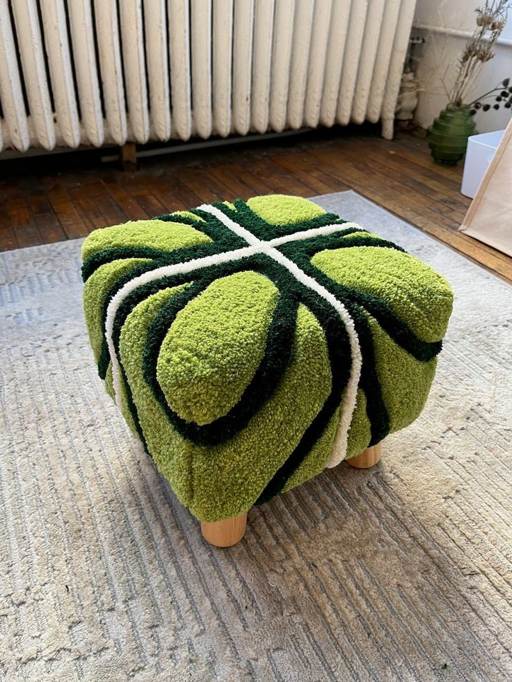 a green and black ottoman sitting on top of a rug next to a radiator