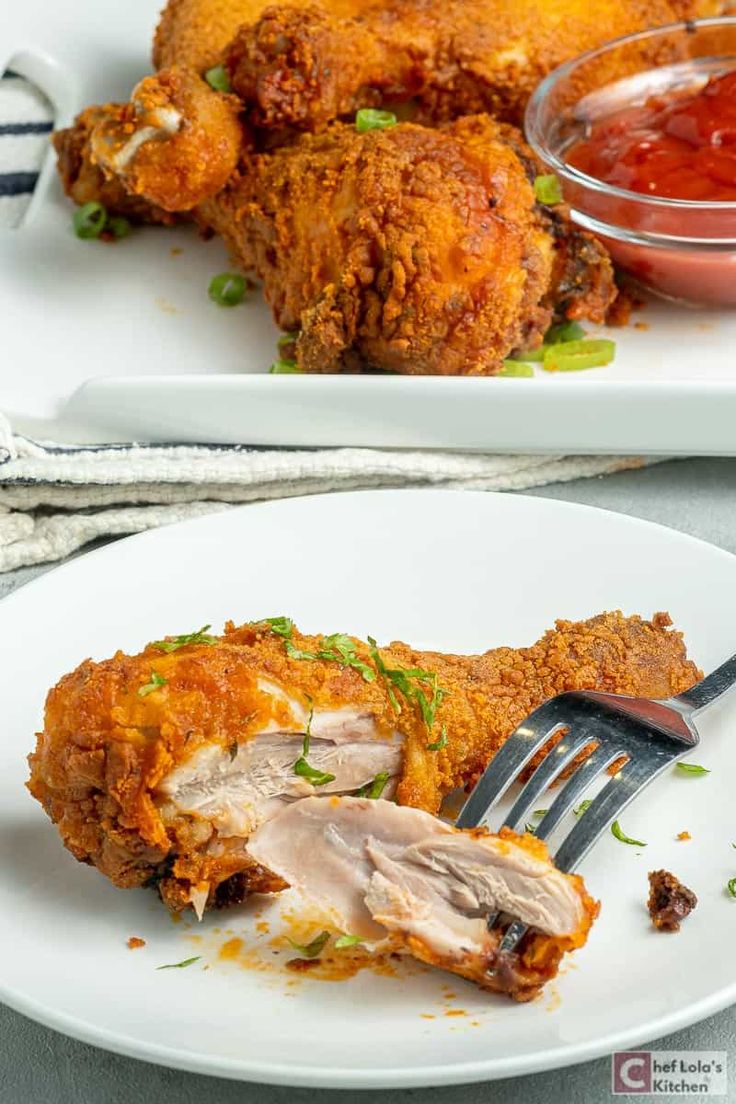 two white plates topped with fried chicken next to a fork and bowl of ketchup