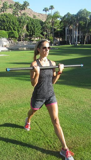 a woman is doing exercises with a barbell in the park on a sunny day