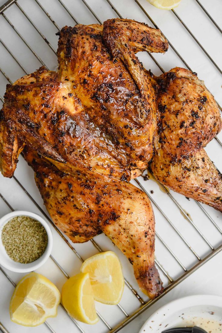 a whole chicken on a grill with lemons and seasoning next to the chickens