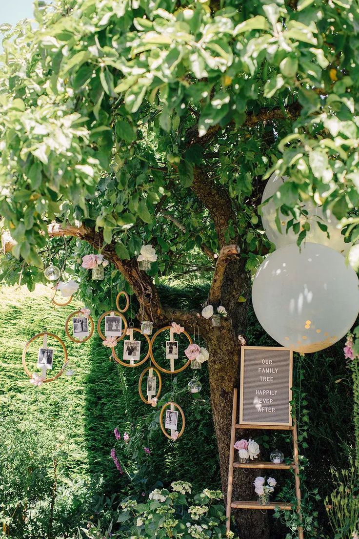 a tree with pictures hanging from it and an easel in the foreground, surrounded by greenery