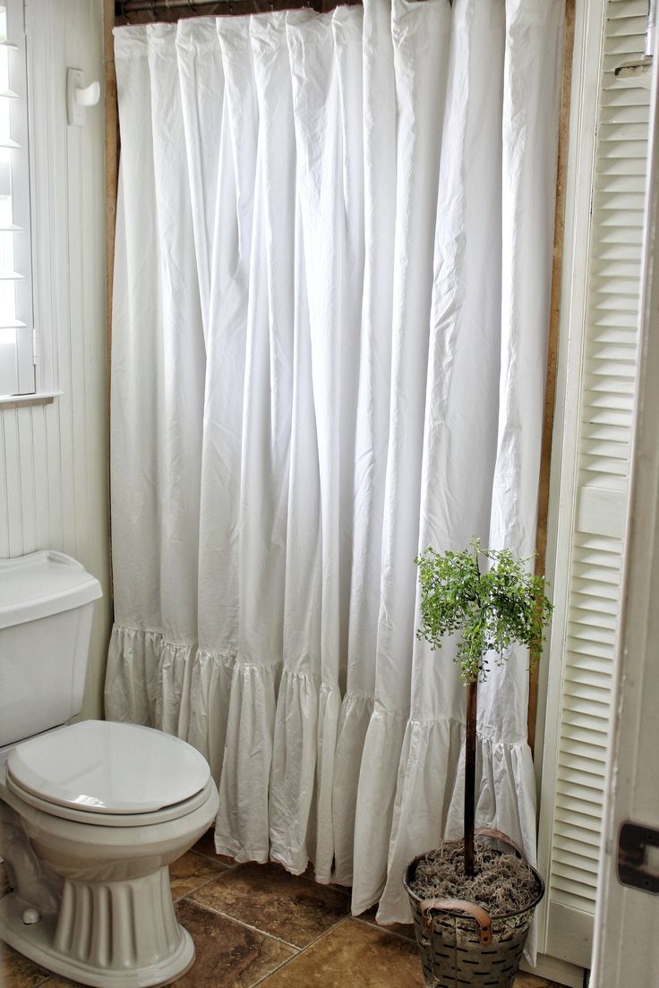 a bathroom with a toilet, shower curtain and potted plant on the floor in front of it