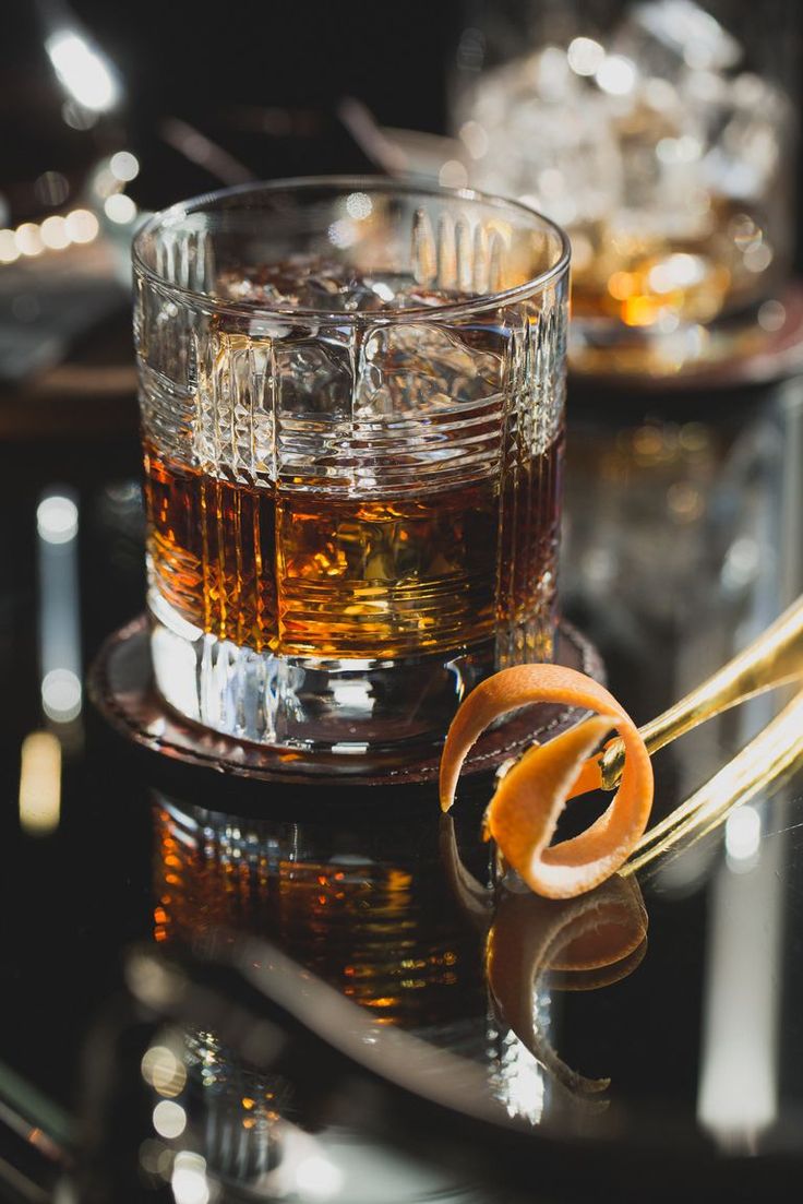 an orange peel sitting on top of a glass filled with alcohol next to two glasses