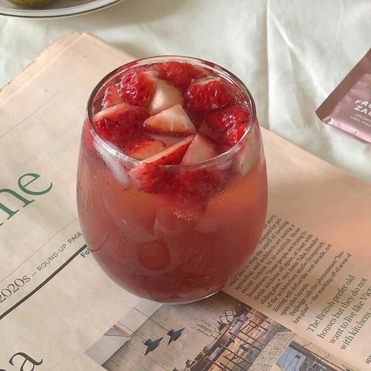 a glass filled with ice and strawberries on top of a table next to a newspaper