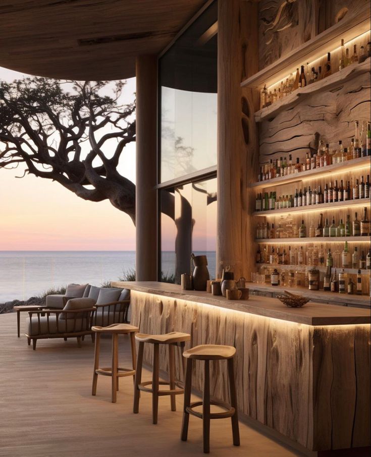 an outdoor bar with wooden stools and shelves filled with bottles on the wall, overlooking the ocean