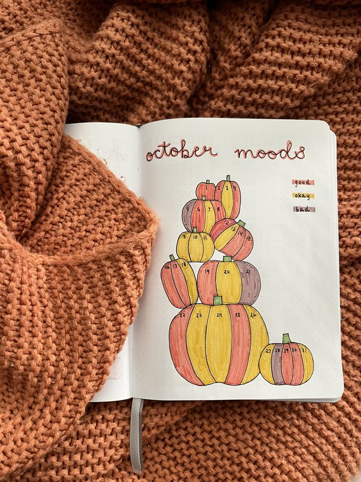 an open book sitting on top of a pile of knitted blankets with pumpkins