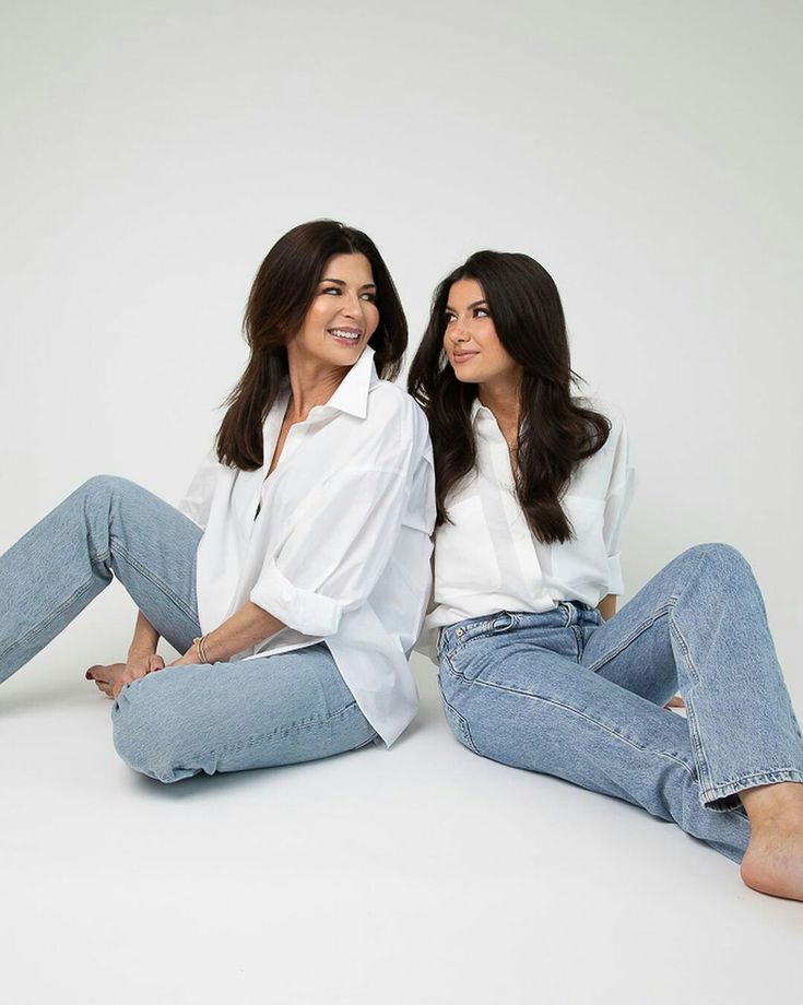 two women are sitting on the floor posing for a photo with their hands in their pockets