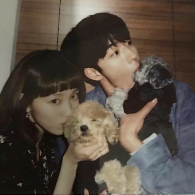 two people holding stuffed animals in their hands and kissing each other while standing next to a wooden wall