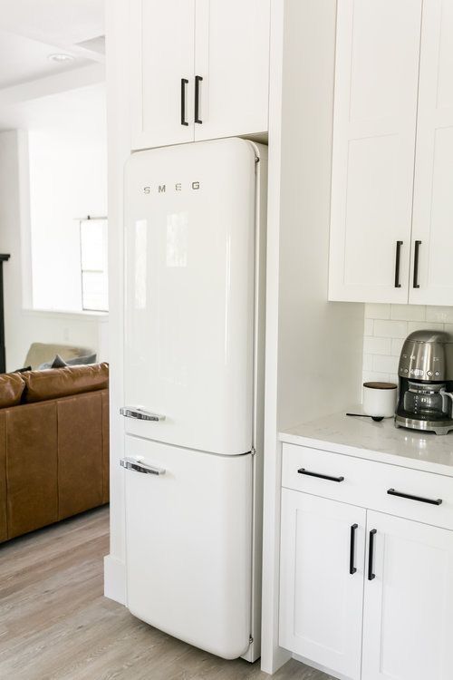 a white refrigerator freezer sitting inside of a kitchen next to a brown leather couch