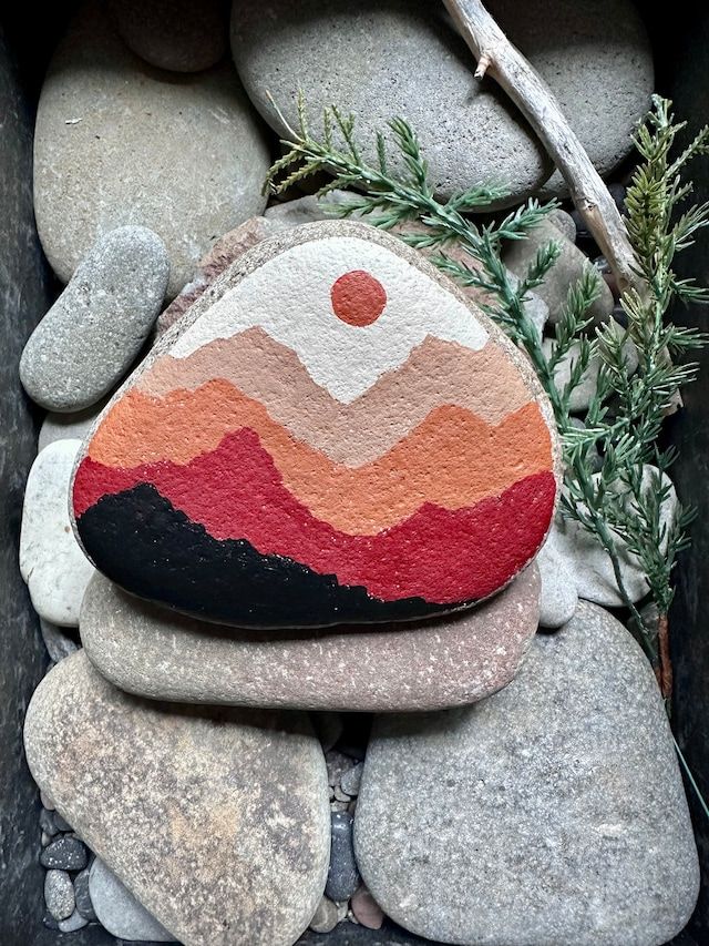 a rock with an orange and red painted on it sitting next to some rocks near a branch