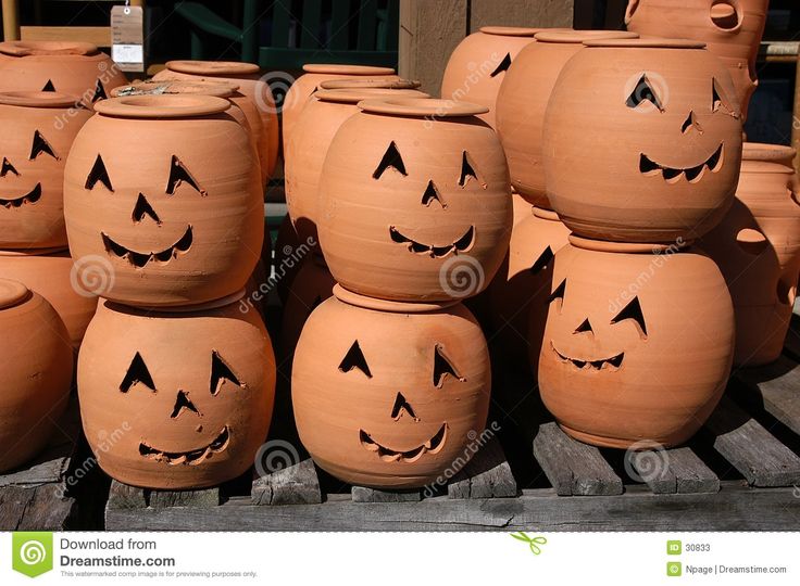 many clay pots with faces drawn on them are stacked up and ready to be used as planters