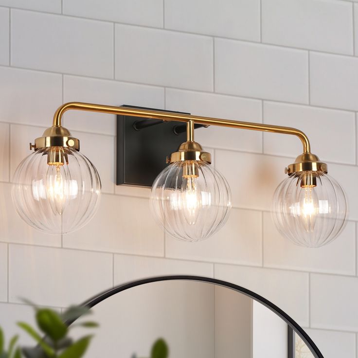 a bathroom light with three clear globes on the wall next to a mirror and potted plant