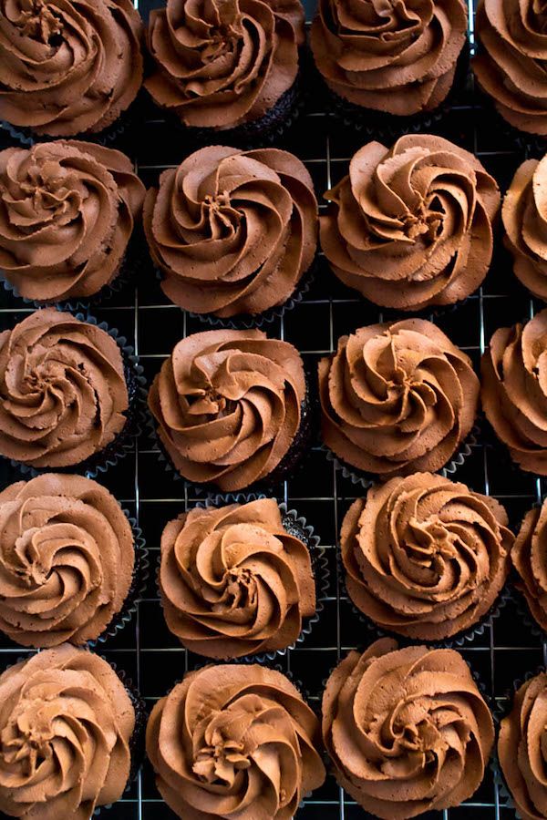 several chocolate cupcakes on a cooling rack with frosting swirled in the middle