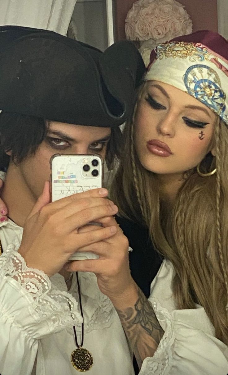 a man and woman dressed in pirate costumes looking at their cell phones while they both look into the camera