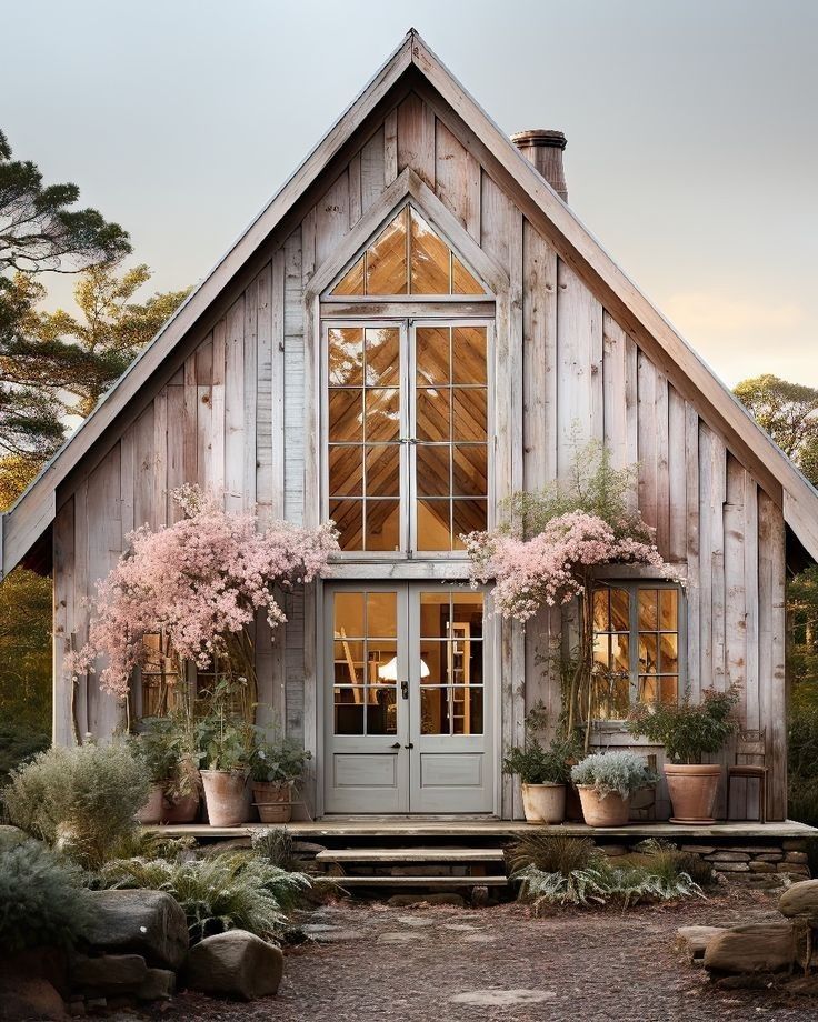 a small wooden house with potted plants and flowers on the front porch, along with stone steps leading up to it