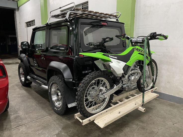 a green and black motorcycle parked in a garage next to a red car on a lift