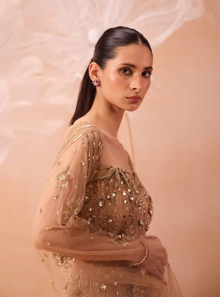 Discover a dreamy all-gold gown adorned with exquisite floral hand-embroidered motifs and shimmering zari sequins. The cape sleeves add an extra layer of elegance, making this gown a stunning choice for any special occasion. Hand Embellished Floor-length Evening Dress For Reception, Hand Embellished Floor-length Embroidered Dress For Festive Occasions, Embellished Embroidered Maxi Dress For Reception, Glamorous Eid Dresses With Zari Work, Evening Gown With Resham Embroidery In Organza, Anarkali Evening Dress With Resham Embroidery For Wedding, Evening Gown With Resham Embroidery On Organza, Embellished Floor-length Embroidered Dress For Reception, Embellished Floor-length Dress For Reception